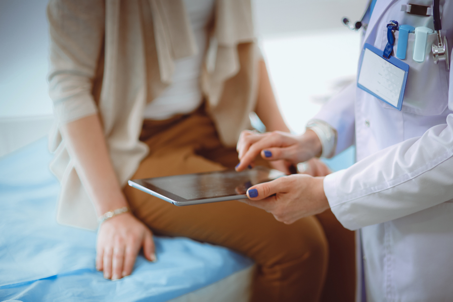Una doctora muestra a una mujer sentada en una camilla los resultados de alguna prueba a través de la pantalla de una tablet