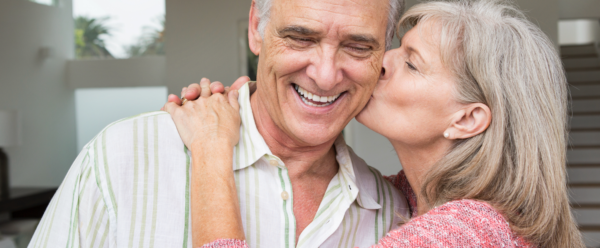 Una mujer mayor abraza y besa en la mejilla a un hombre de edad similar que sonríe ante el gesto