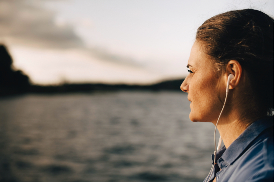Una mujer que tiene en las orejas unos auriculares contempla el mar absorta en sus pensamientos
