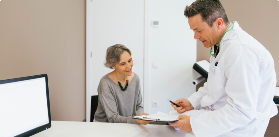 Un doctor en una consulta charla de manera informal con una paciente mientras le muestra un informe impreso en papel