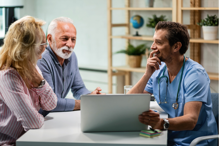 Un doctor dialoga amigablemente en su consulta con un hombre y una mujer mayores mientras ven una tablet